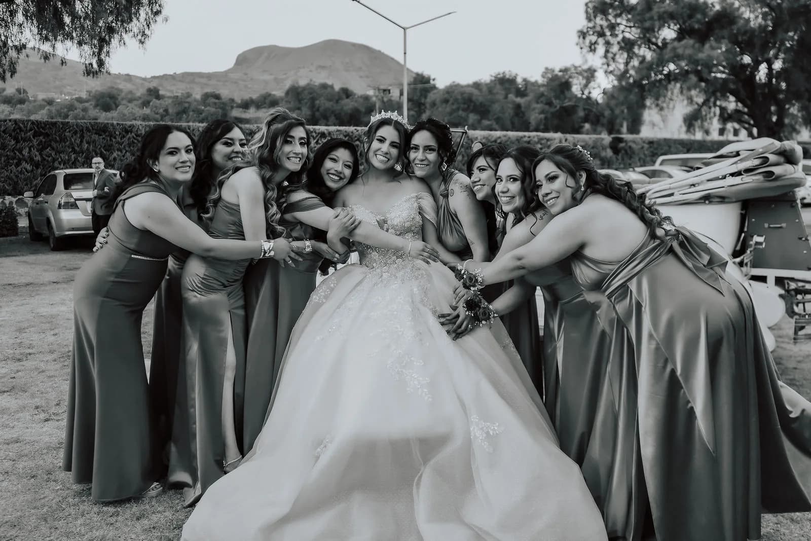 Novia con tiara abrazada por sus damas de honor con vestidos de satín en el jardín de su boda.